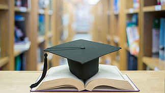 Graduation cap over open books in a library room.