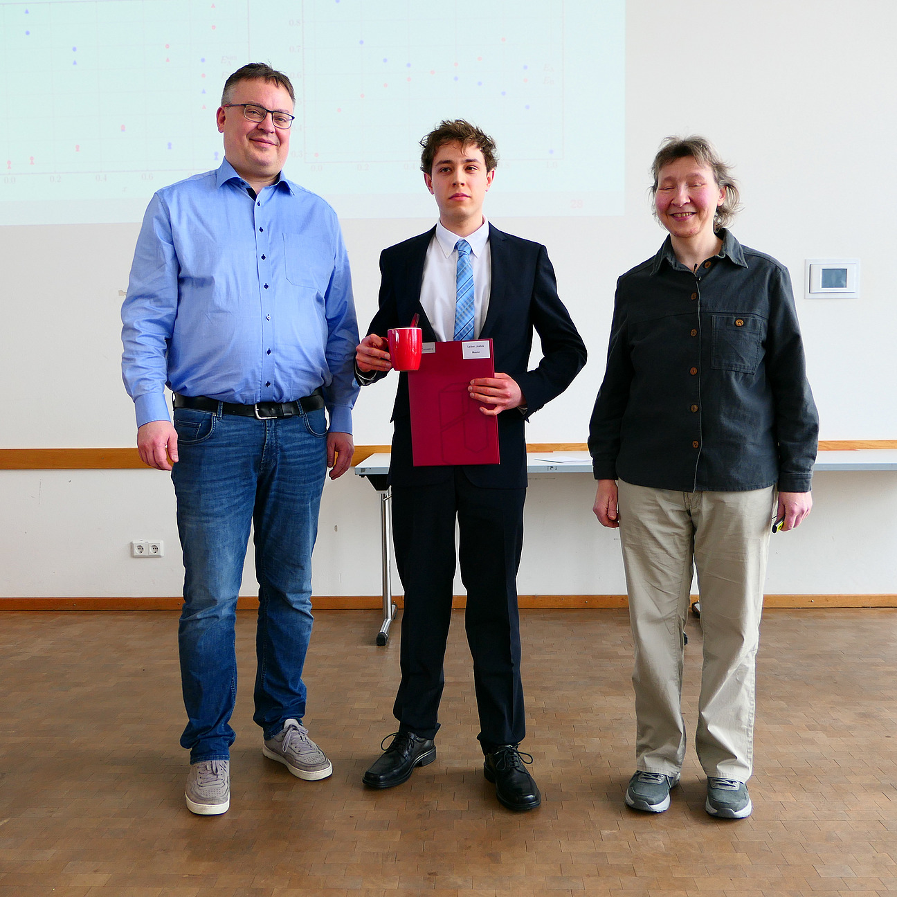 Ein Student steht mit seinem Abschlusszeugnis zwischen Dekan und Studiendekanin.