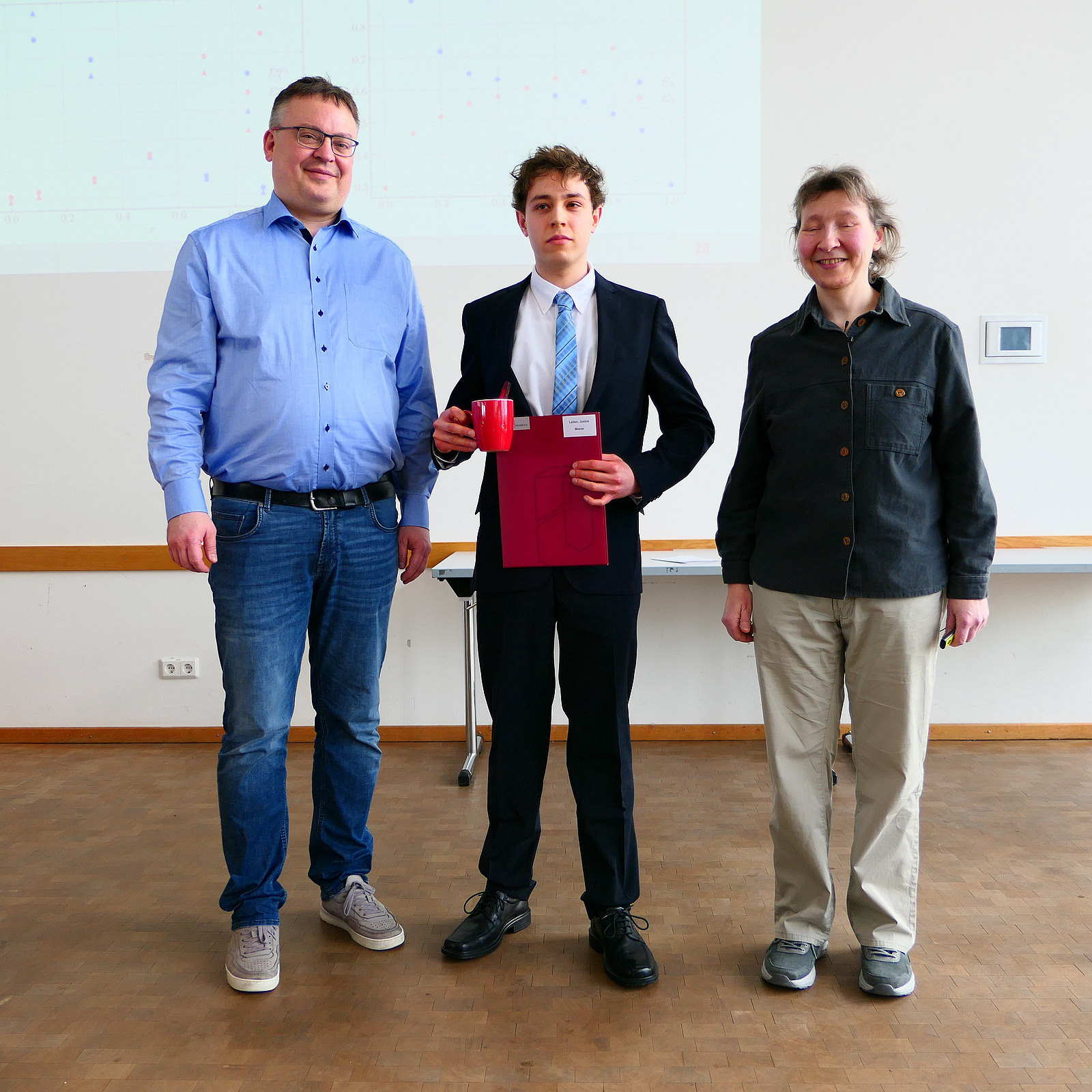 Ein Student steht mit seinem Abschlusszeugnis zwischen Dekan und Studiendekanin.