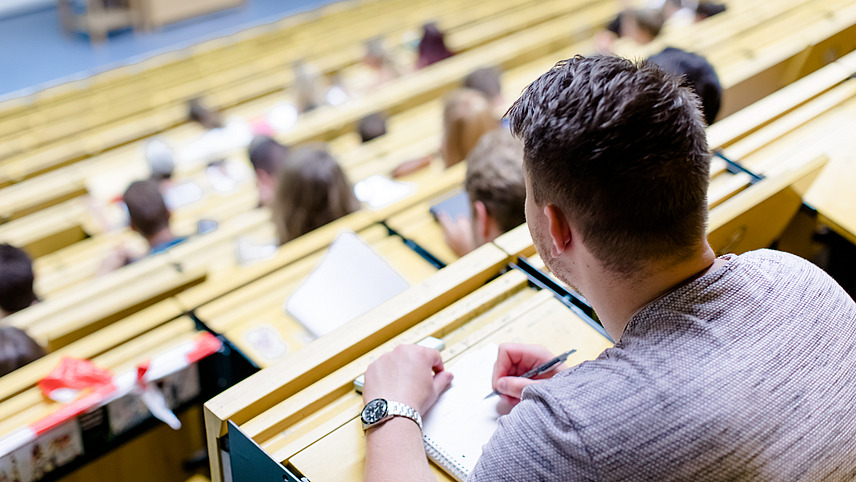 Looking across the rows of seats in a lecture hall at students taking notes during the lecture.