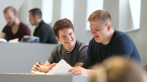 Studierende sitzen im Arbeitsbereich am Tisch in einem Vorlesungsgebäude