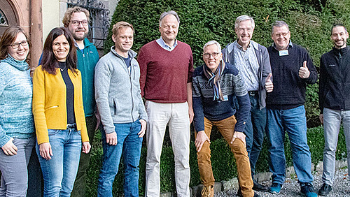 A group of nine people smiles happily at the camera