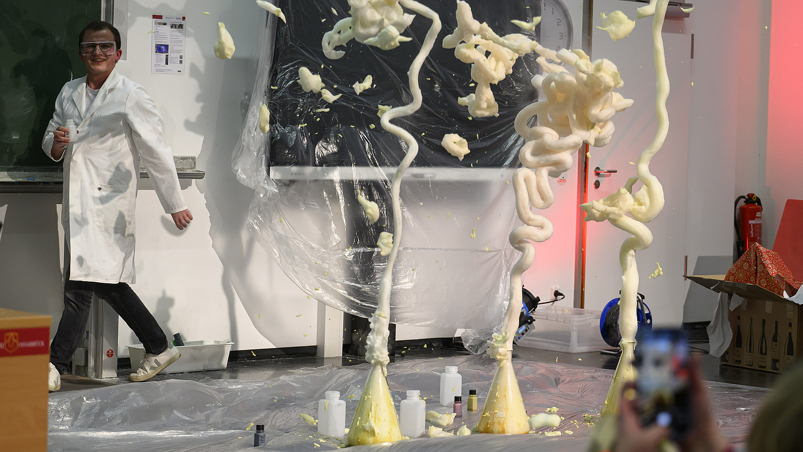 Person in wei&szlig;em Kittel unternimmt chemische Experiment, Schaum fliegt durch die Luft