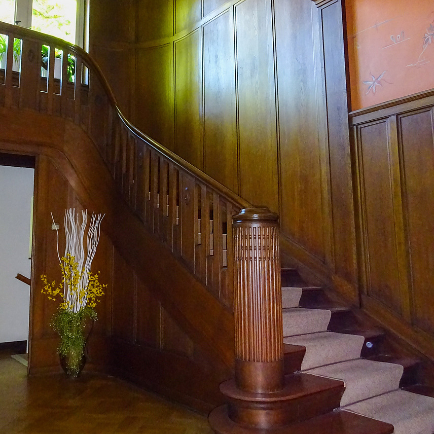 Stylish and light-flooded staircase, with wooden stairs and numerous wooden wall elements as well as large window front on the gallery.