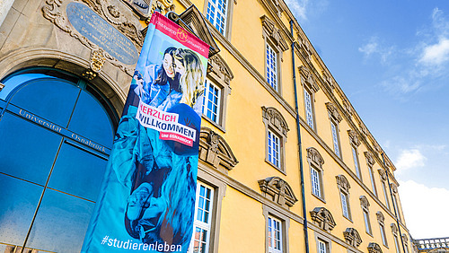 Eine Werbefahne mit dem Slogan "Sch&ouml;n dass ihr da seid" vor dem Eingang des Schlosses.