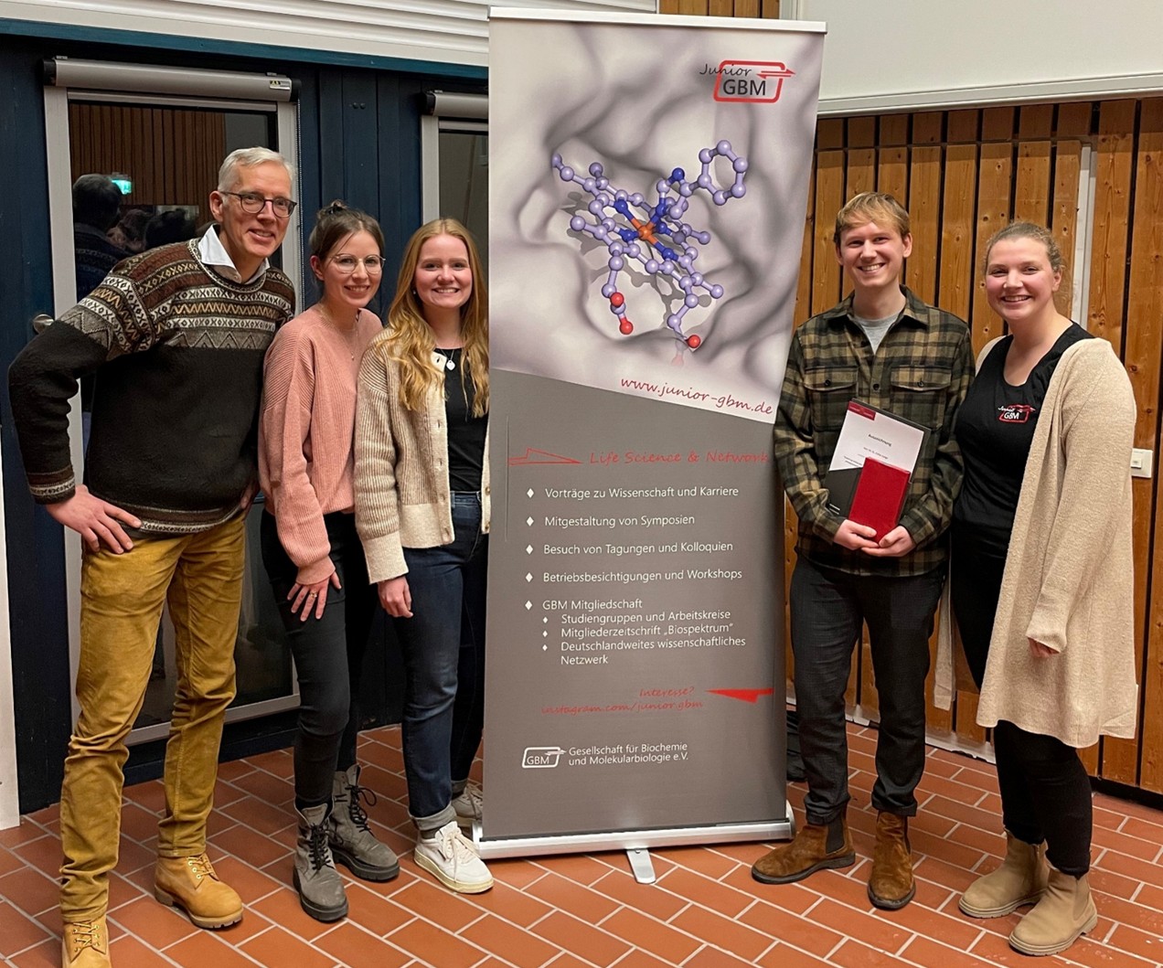 Five smiling persons, the second from the right is holding documents