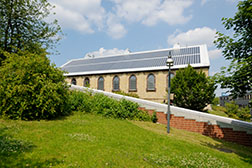 Gebäude 66 in der Barbarastraße 12  beheimatet das Institut für Umweltsystemforschung USF. Gebäudeansicht Seitlich. Mauer und Wiese im Vordergrund. Blick auf das Dach des Gebäudes mit der Photovoltaikanlage.