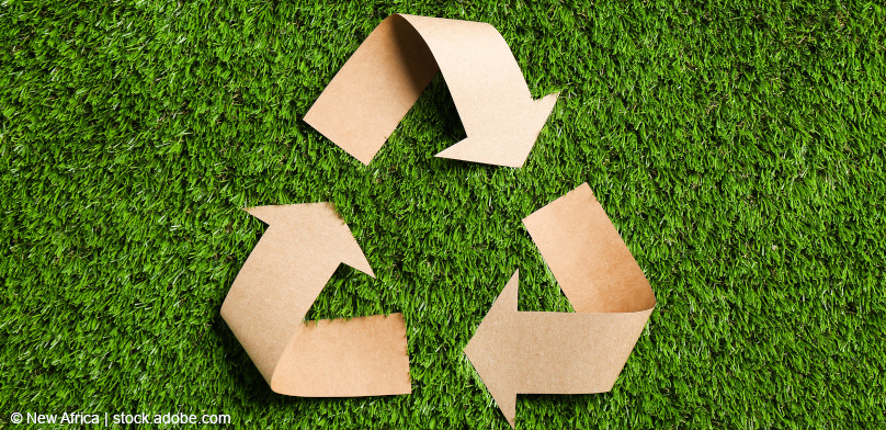 Aus Kraftpapier ausgeschnittenes Recycling-Symbol auf grünem Gras, Draufsicht