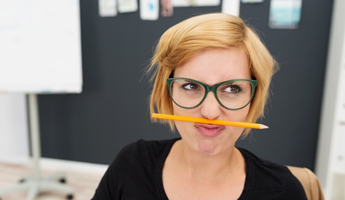 Junge Frau mit Brille denkt nach und hat dabei einen Stift zwischen Mund und Nase eingeklemmt. Foto: contrastwerkstatt/Fotolia