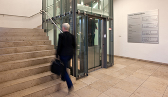 Ein Mann mit einer Aktentasche geht in einem Universitätsgebäude eine Treppe hinauf. Er ist dabei nur verschwommen zu sehen und befindet sich demnach in Bewegung. Foto: Stephan Schute