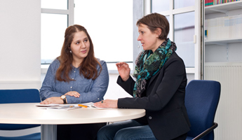 Zwei Frauen sitzen nebeneinander an einem runden Tisch und befinden sich in einem Beratungsgespräch. Vor ihnen sind Informationsbroschüren zu sehen. Foto: Stephan Schute
