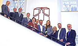 Vertreterinnen und Vertreter von Universität, regionalen Unternehmen, IHK sowie Stadt und Landkreis stehen auf Treppe vor Universitäts-Logo