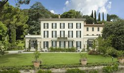 Ansicht der Villa (Deutsch-italienisches Zentrum für den Europäischen Dialog) mit sie umgebenden Garten und grünen Bäumen, darüber blauer Himmel.