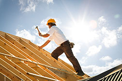 Zimmermann arbeitet kurzärmlig auf einem Dach in der Sonne