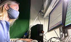 Frau mit Mundschutz bei der Beobachtung der Gehirnsignale eines schlafenden Teilnehmers im Labor