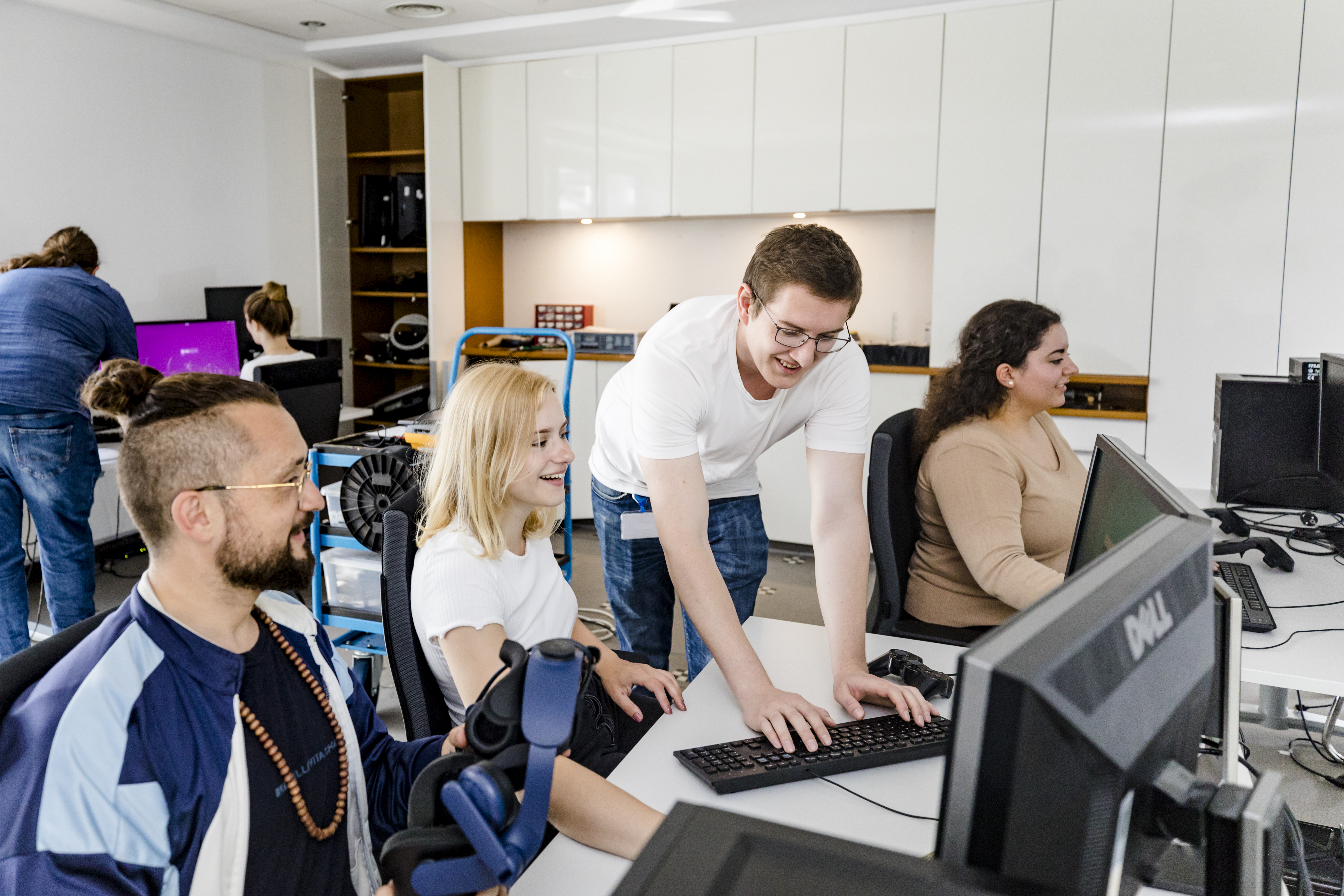 Mehrere Studierende arbeiten an PCs und lachen