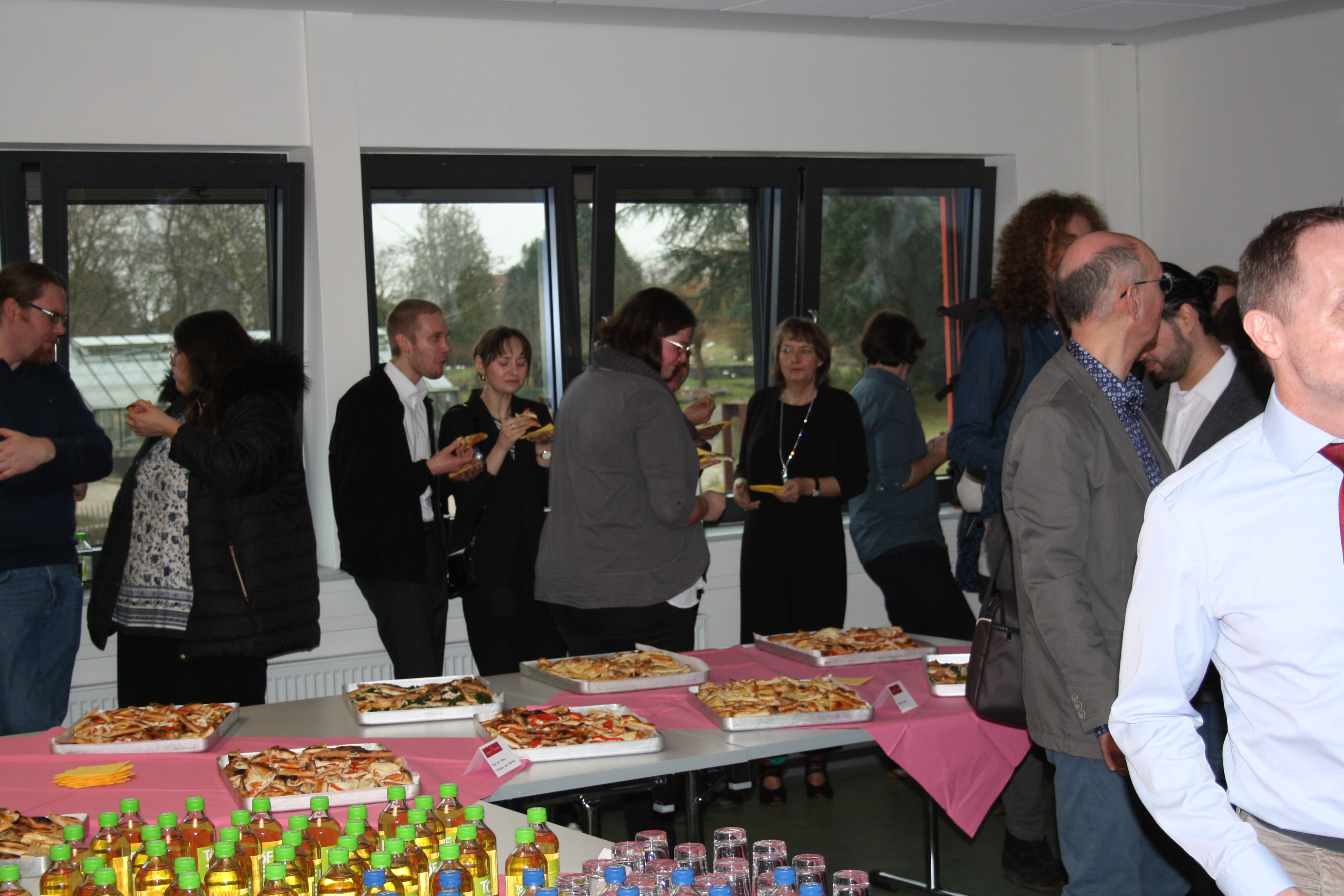 Several people stand in front of and behind a table with finger food.