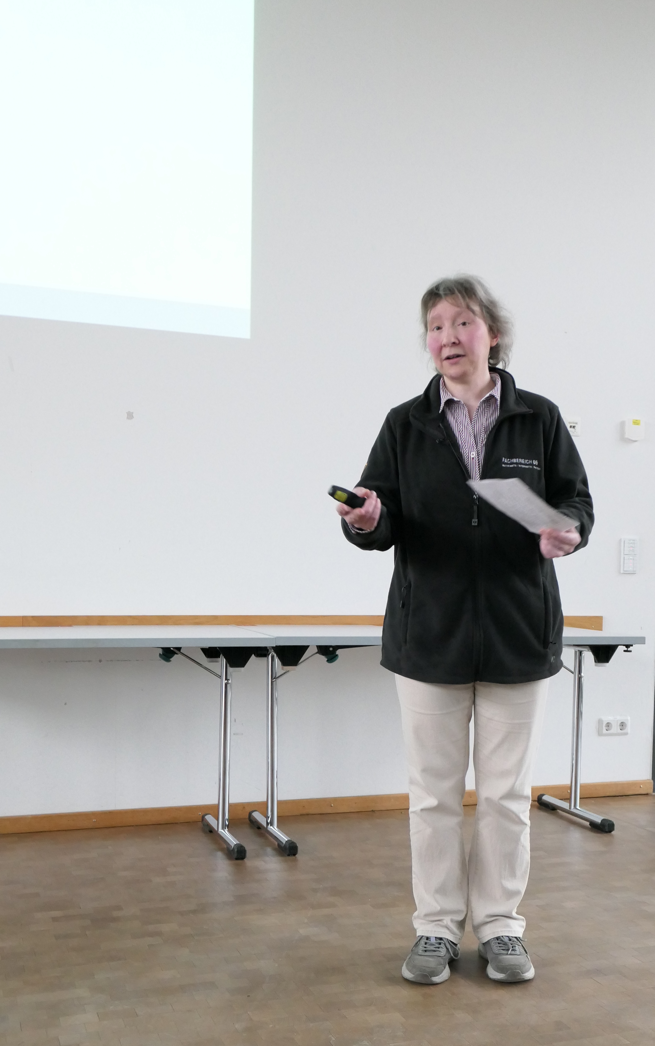 The Dean of Studies stands in front of a white wall with a sheet of paper in her hand.