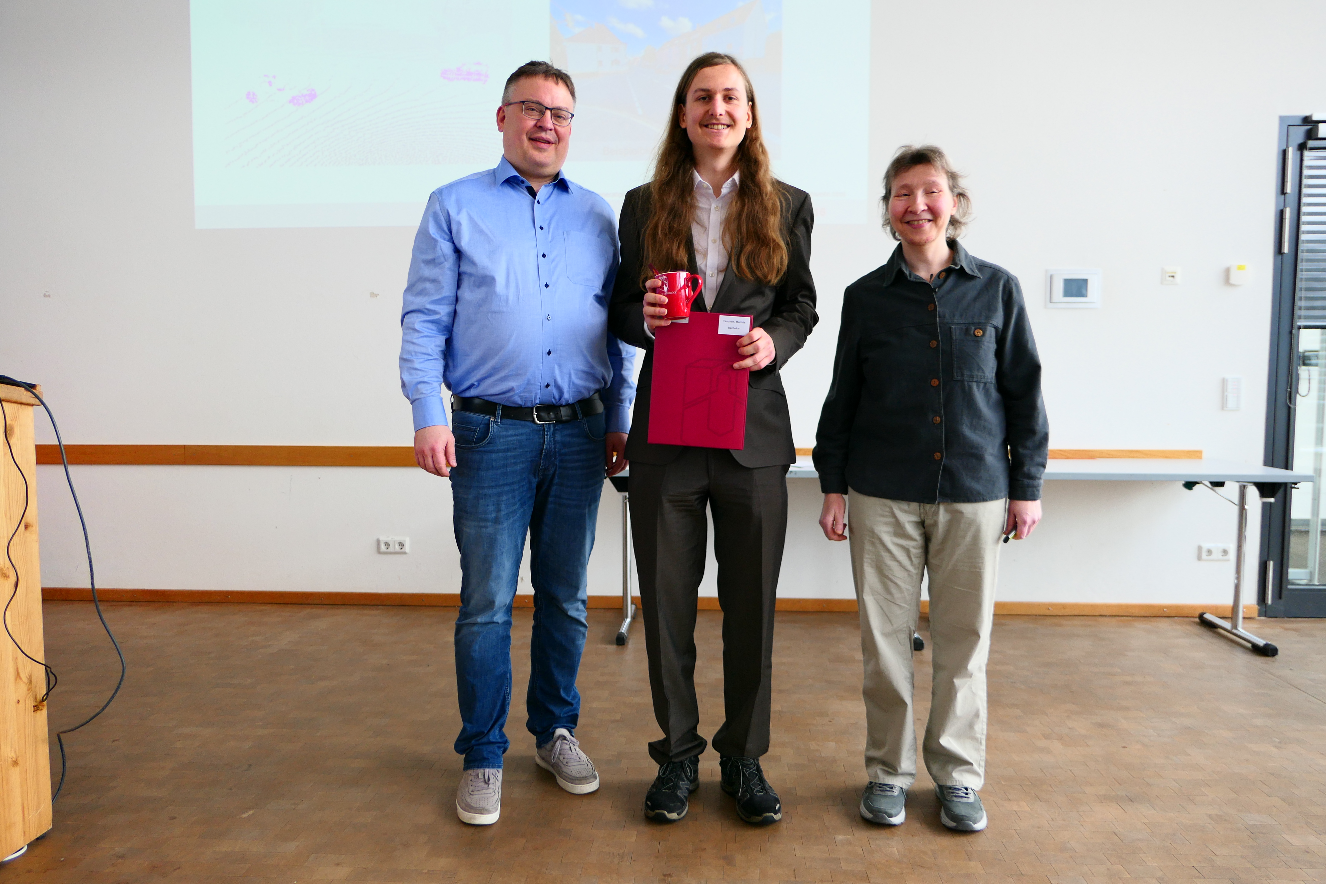 Ein Student steht mit seinem Abschlusszeugnis zwischen Dekan und Studiendekanin.