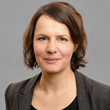 Porträt einer Frau mit schulterlangen braunen Haaren, sie trägt ein dunkles Sakko und lächelt leicht.